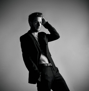 他把手放进口袋里,在灰色背景上摆出侧身姿势.闭合照片