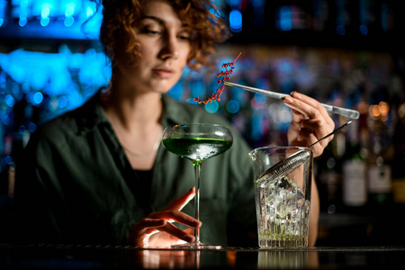 酒吧里的年轻女子拿着盛着鸡尾酒的玻璃杯，小心翼翼地装饰着