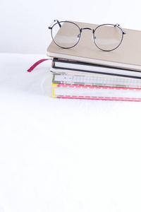一摞笔记簿，上面有一张白色的桌子，上面有一副眼镜。