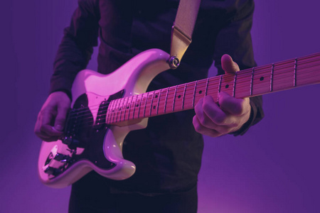年轻的白人音乐家在紫色背景的霓虹灯下弹吉他