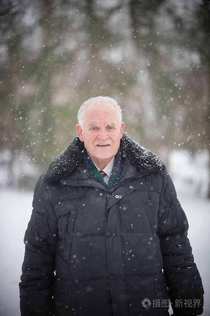 一个穿着羽绒服站在冬天森林里的老人