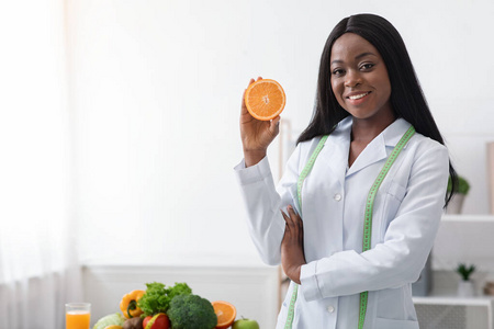 积极的黑人女营养师拿着橙色的一半
