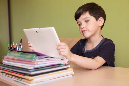 冠状病毒隔离期间，男孩一边做作业一边用平板电脑。远程教育理念。