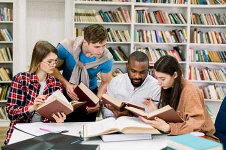 聪明自信的多民族青年学生在大学图书馆边看书找资料一起学习