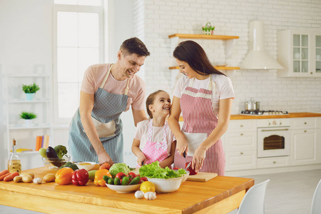 快乐的家庭和孩子在厨房的桌子上准备新鲜蔬菜。