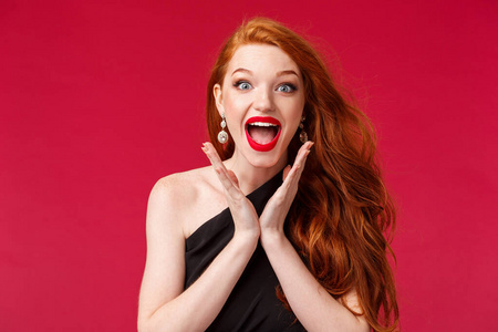 用红色唇膏和黑色礼服贴近兴奋美丽年轻红头发女人的手,拍手热情,笑