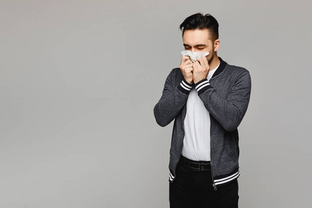 手帕纸年轻人打喷嚏,用餐巾纸捂住嘴,灰色背景,与世隔绝.