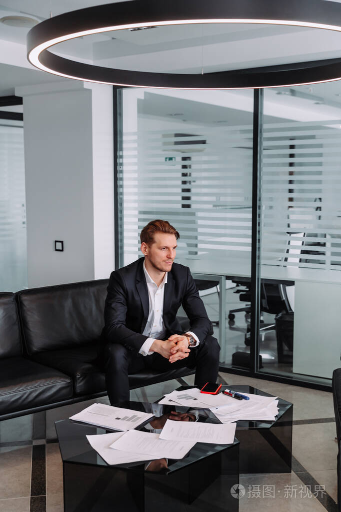 帅气时尚自信的商人穿着漂亮的西装坐在办公室的沙发上