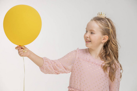 一个可爱的金发小女孩，穿着粉红色的裙子，拿着一个气球在一个浅色的背景上，节日概念氦球