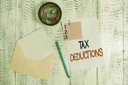 文字写作文本税收减免。企业理念为减少可征税费用的收入信封纸便笺圆珠笔夹持器木质背景。