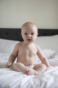 穿着尿布的可爱宝宝坐在床上看着摄像机
