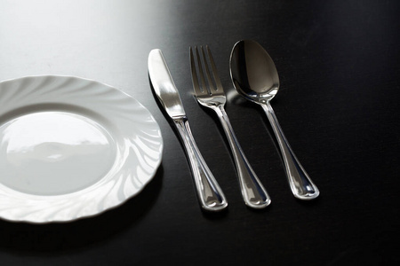 黑色背景的餐具。叉子，勺子，刀，盘子。