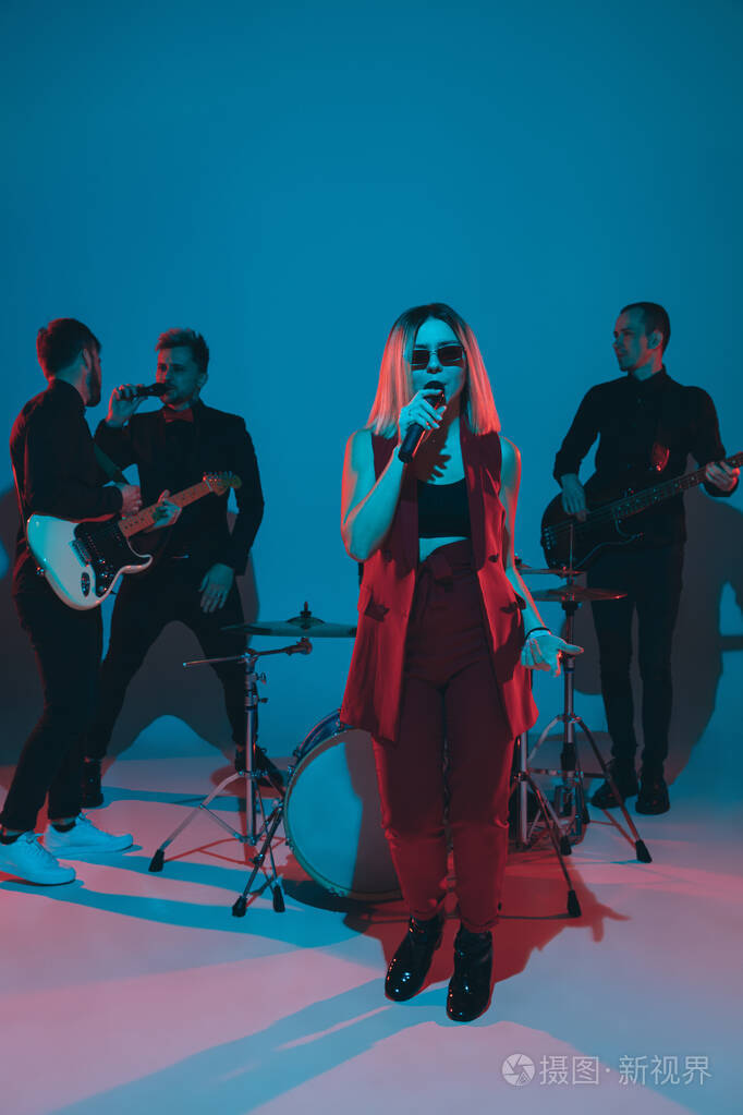 年轻的白人音乐家,乐队在蓝色工作室背景上霓虹灯下表演,歌手在前面照