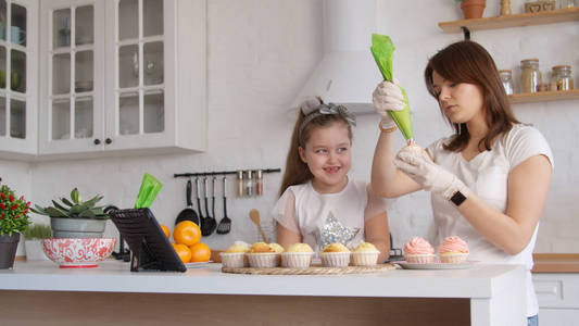 Young mother and little daughter icing cupcakes 