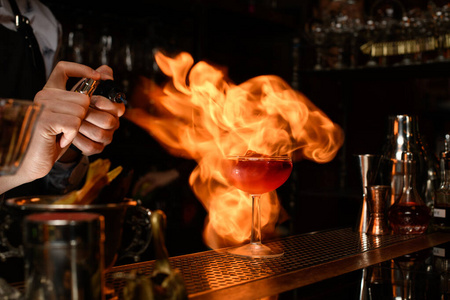 酒保专业地将鸡尾酒洒在玻璃杯上，然后点燃。