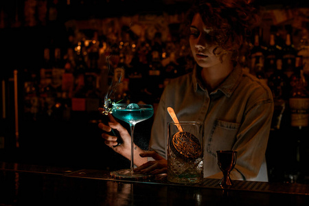 黑暗酒吧里的年轻女子开始用蓝色饮料在酒杯上生火。