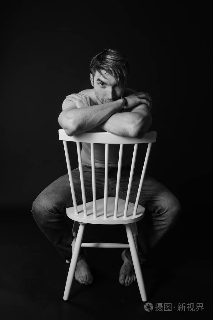 肌肉发达身材健美的年轻健美男模特在椅子上摆姿势黑白照片