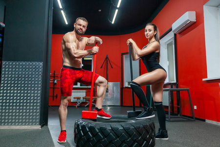 全身肌肉强壮的男人和性感的健身女人在健身房用大锤和轮胎摆姿势
