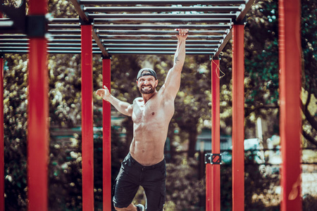 在一个阳光明媚的日子里，一个长着胡须的健美运动员在户外的现代健美操公园里练习上半身