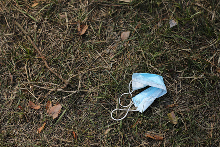 脏兮兮的用过的医用口罩躺在地上,草地在背景上.冠状病毒恐慌.