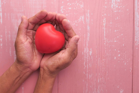 senior woman holding red heart in hands, top view 