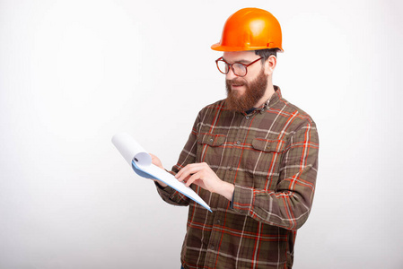 这位年轻的建筑师戴着橙色的安全帽，白色的背景，正在翻阅设计图和文件
