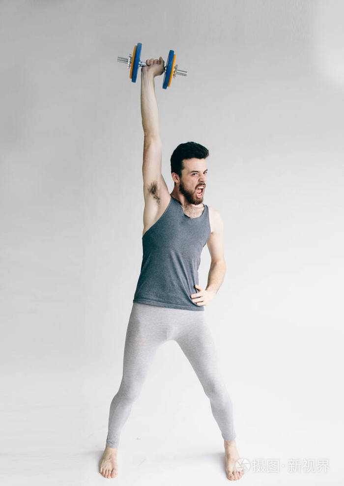 瘦小的男人在训练他的二头肌举一个哑铃的人青年学生培养成才