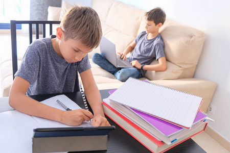 技术教育在线学习家庭远程教育。男孩开始用书本做数学作业，其他男孩在家里用笔记本电脑上在线课
