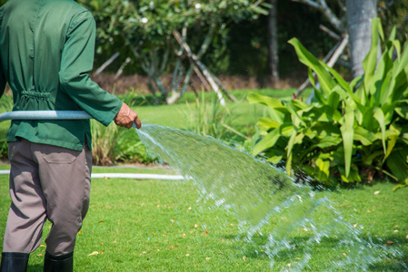 在后院用水管给花园浇水的人