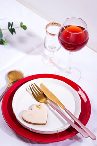 节日餐桌上的餐具和装饰品。盘子红酒杯和餐具，白色纺织品背景上有绿叶。