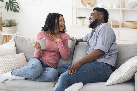 快乐的黑人夫妇坐在家里，喝着咖啡在沙发上休息