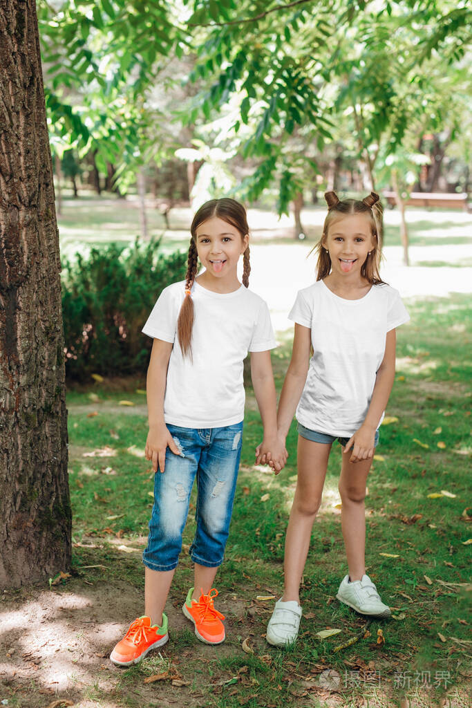 两个穿着白色t恤衫的小女孩手牵着手站在户外公园里模型