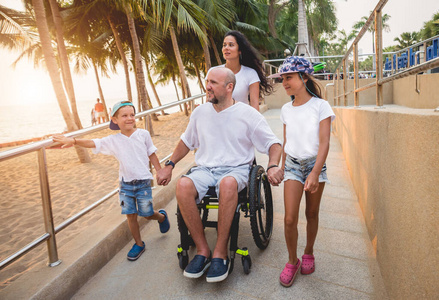 坐轮椅的残疾人和家人一起在斜坡上走向海滩。