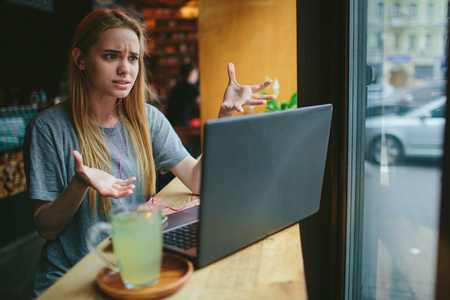 一个年轻的金发女郎在咖啡馆里用笔记本电脑工作。她不知所措。桌子上有一杯绿茶。