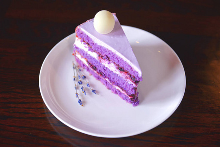 一片紫色薰衣草蛋糕,上面有浆果和熏衣草花,放在白色盘子里.照片