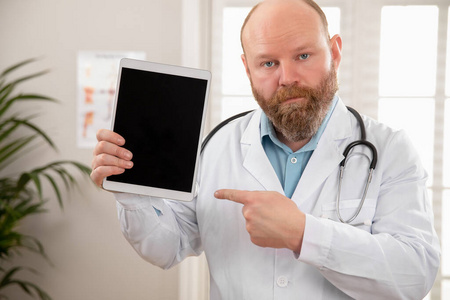 严肃的成年男性医生在平板电脑上显示数字图像或报告