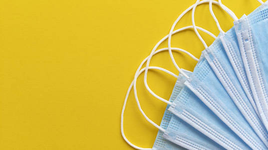 黄色背景的蓝色医用口罩.带复印空间的简易平铺.医学概念.库存照片.