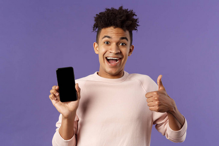 快乐的年轻人，害怕的西班牙裔人推荐应用程序，在线送货服务或食品订单，竖起大拇指，微笑兴奋，手持手机，显示智能手机屏幕