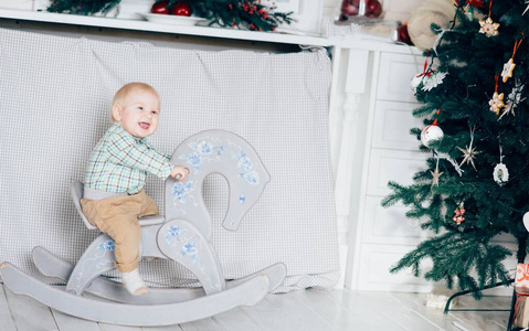 小男孩骑着马在白色的房间里装饰圣诞和寒假。一个人玩，玩得开心。图中绿色圣诞树的一部分