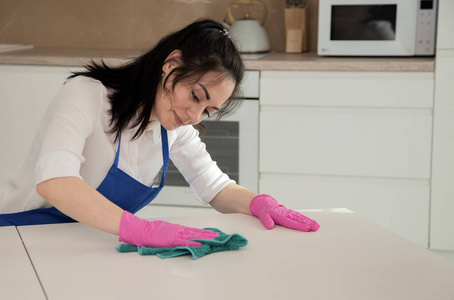 年轻漂亮的黑发女孩在厨房打扫卫生，擦着白桌子的表面。