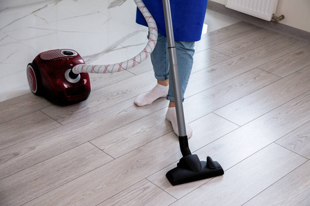 一个穿着牛仔裤和白袜子的女孩正在用吸尘器清扫地板。红色吸尘器。