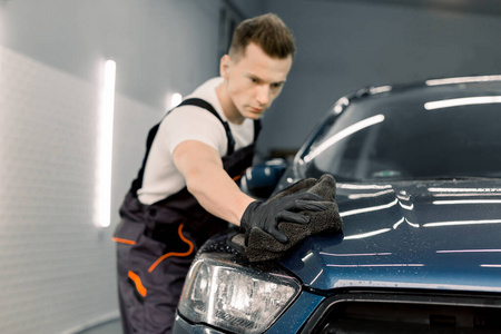汽车细节和清洁概念。男洗车工手拿超细纤维擦拭汽车引擎盖。用超细纤维选择性聚焦在手上。