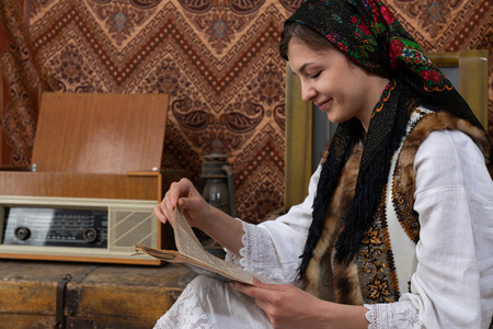 穿着乌克兰民族服装的快乐年轻女子坐在复古复古的房间里看旧报纸