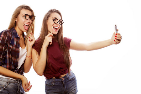 两个戴着派对眼镜的快乐年轻女人在白色背景下用手机自拍