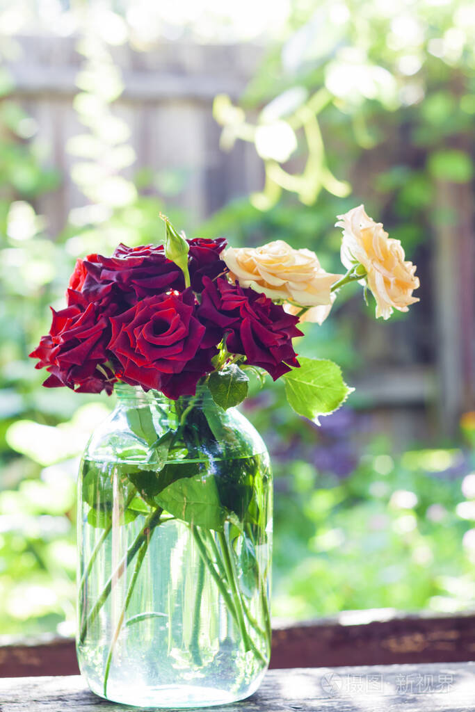 在模糊的绿色花园背景上的玻璃瓶里的复古玫瑰花束