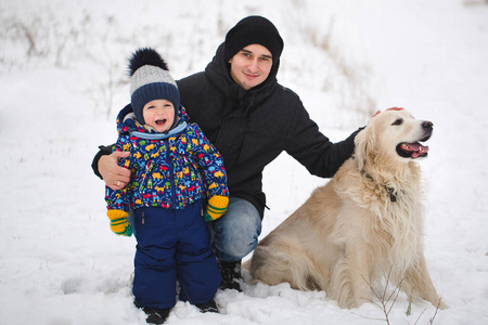 爸爸和儿子在雪地里和狗玩。金毛猎犬