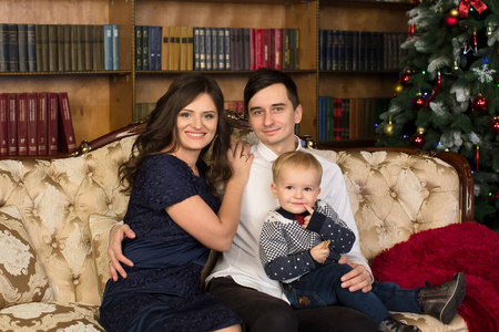 家庭。爸爸，妈妈和小儿子坐在圣诞树旁的沙发上。