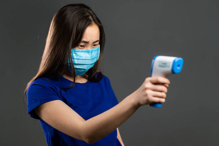 戴着医用防护面罩的美丽亚洲女人用电子温度计测量体温。流感流行，Covid19，冠状病毒。