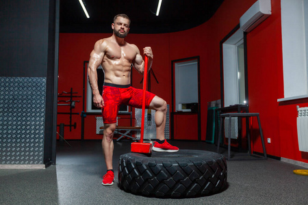 运动型肌肉男的全长肖像，在健身房里摆着大锤和轮胎准备运动