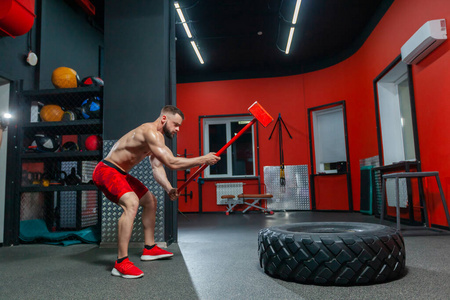 在现代健身房里进行大锤训练的强壮肌肉男子的全长肖像
